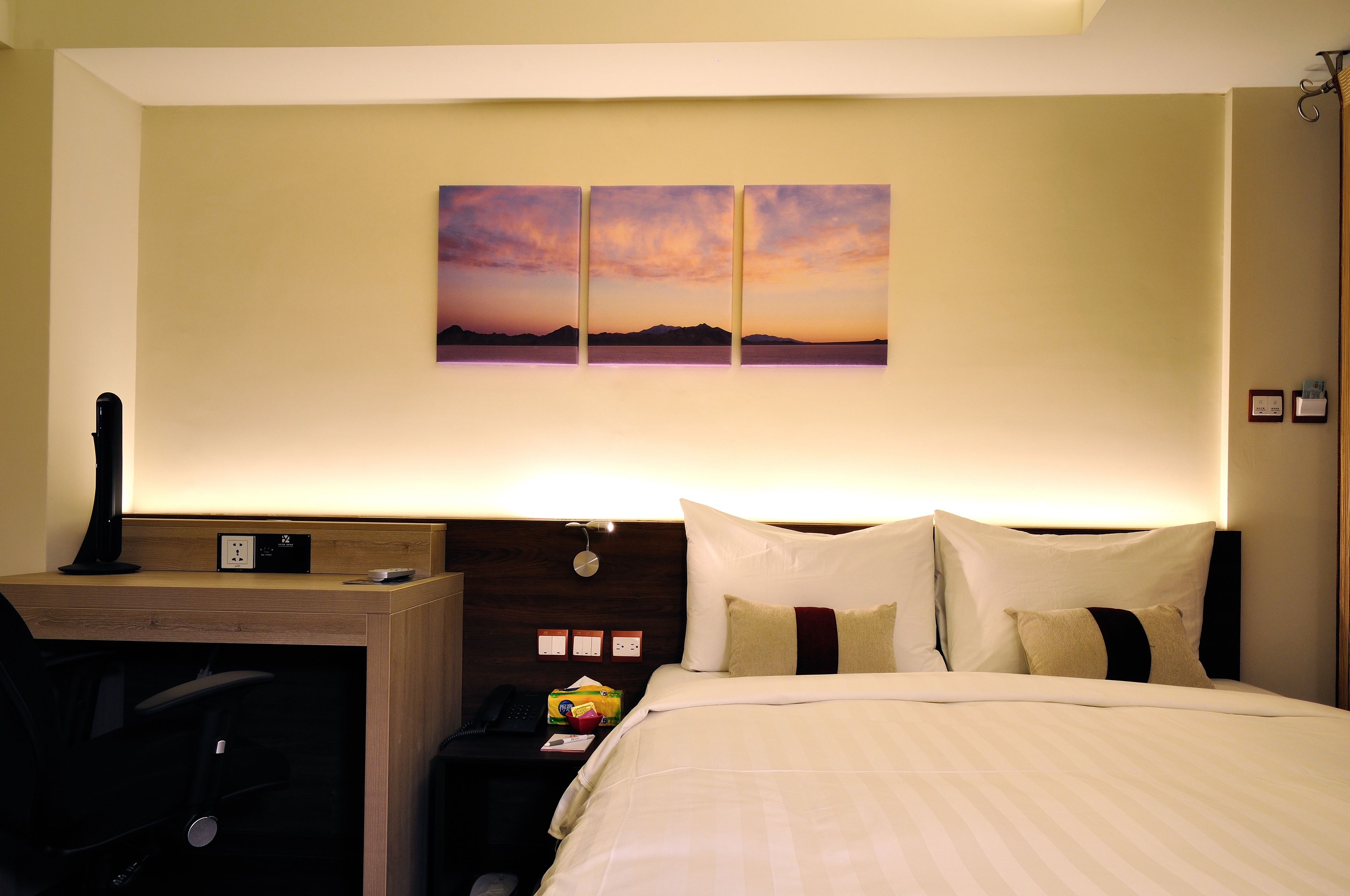 A hotel room with a bed, a desk, and a wall-mounted artwork.