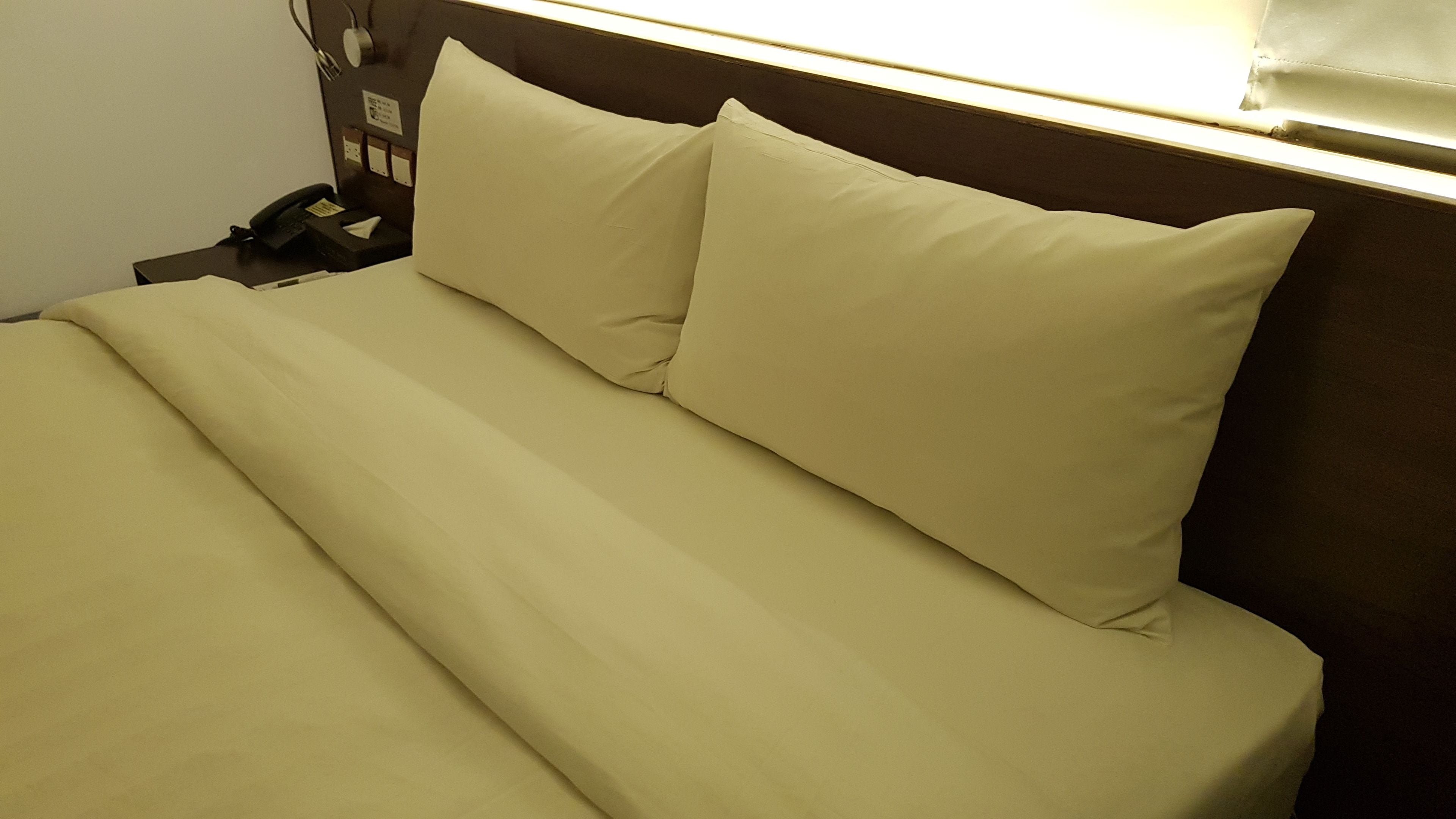 A bed with a headboard and a nightstand with a phone and a lamp.