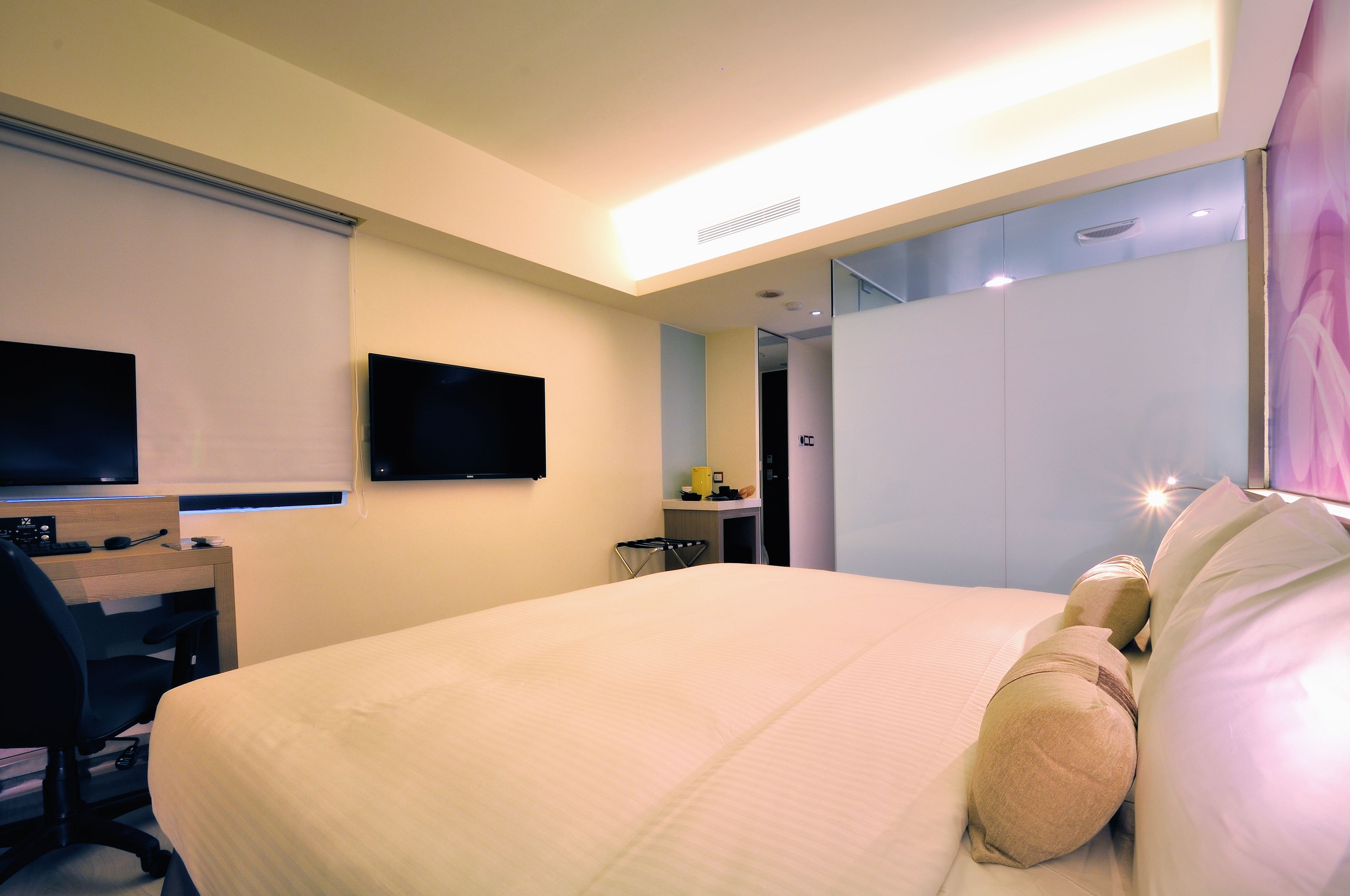 A hotel room with a bed, a desk with a chair, a television, and a wardrobe.