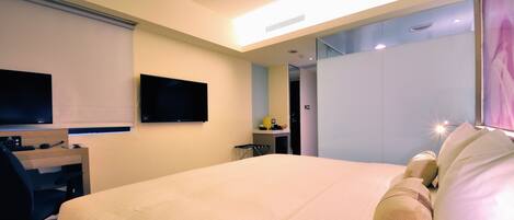 A hotel room with a bed, a desk with a chair, a television, and a wardrobe.