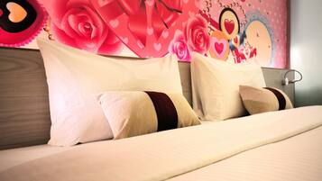Een net opgemaakt bed met witte en beige kussens, een houten hoofdbord en een muur versierd met roze rozen en harten.