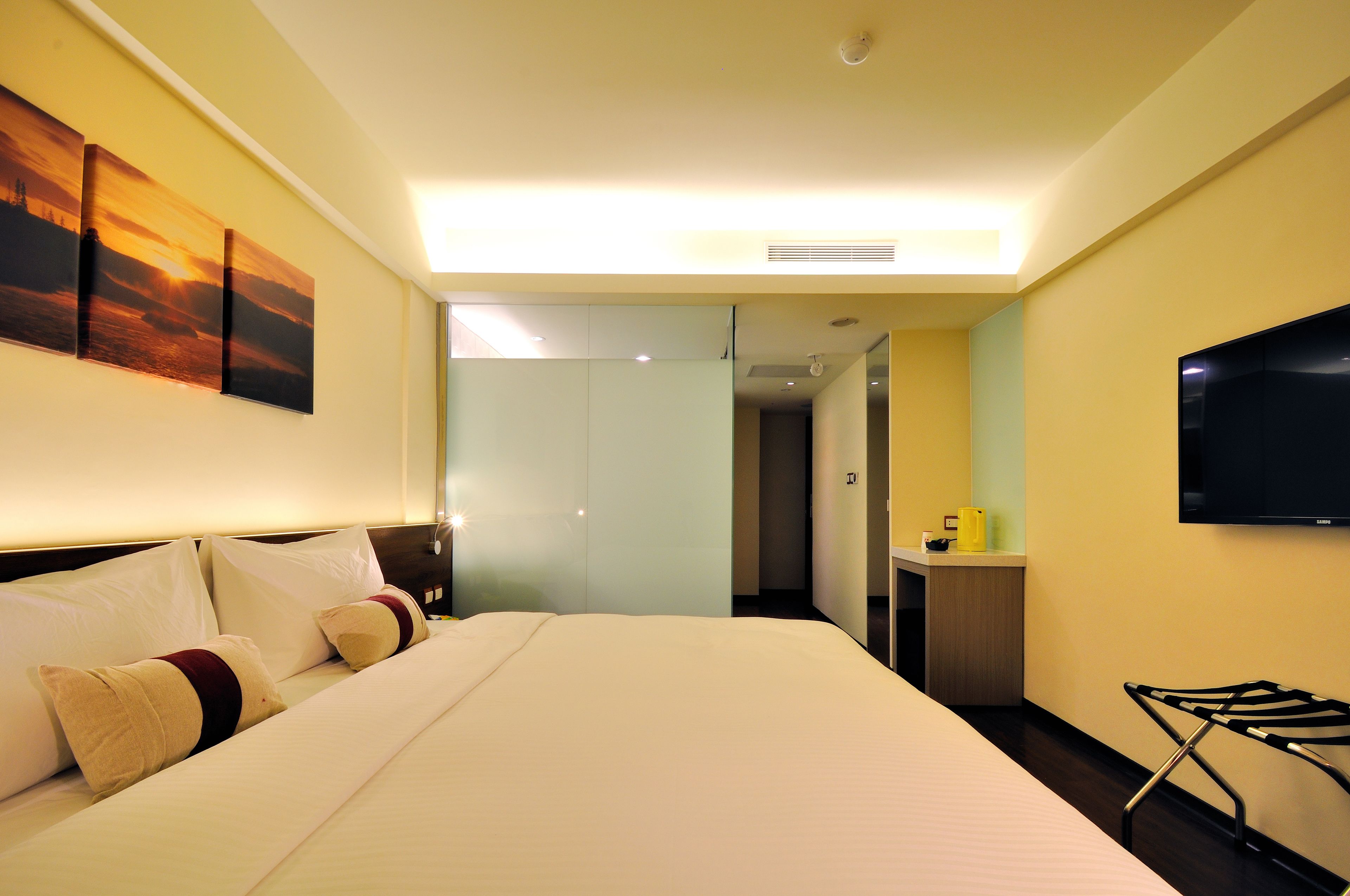 A hotel room with a bed, a flat-screen TV, a desk with a chair, and a painting on the wall.