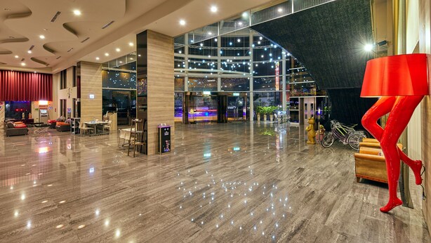 A spacious lobby with a high ceiling, a seating area with sofas and chairs, a large red sculpture, and a glass entrance leading to an outdoor area. - Freedom Design Hotel (Taoyuan City)