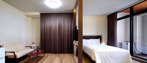 A hotel room with a bed, a sofa, a small table with a vase, and a large window.