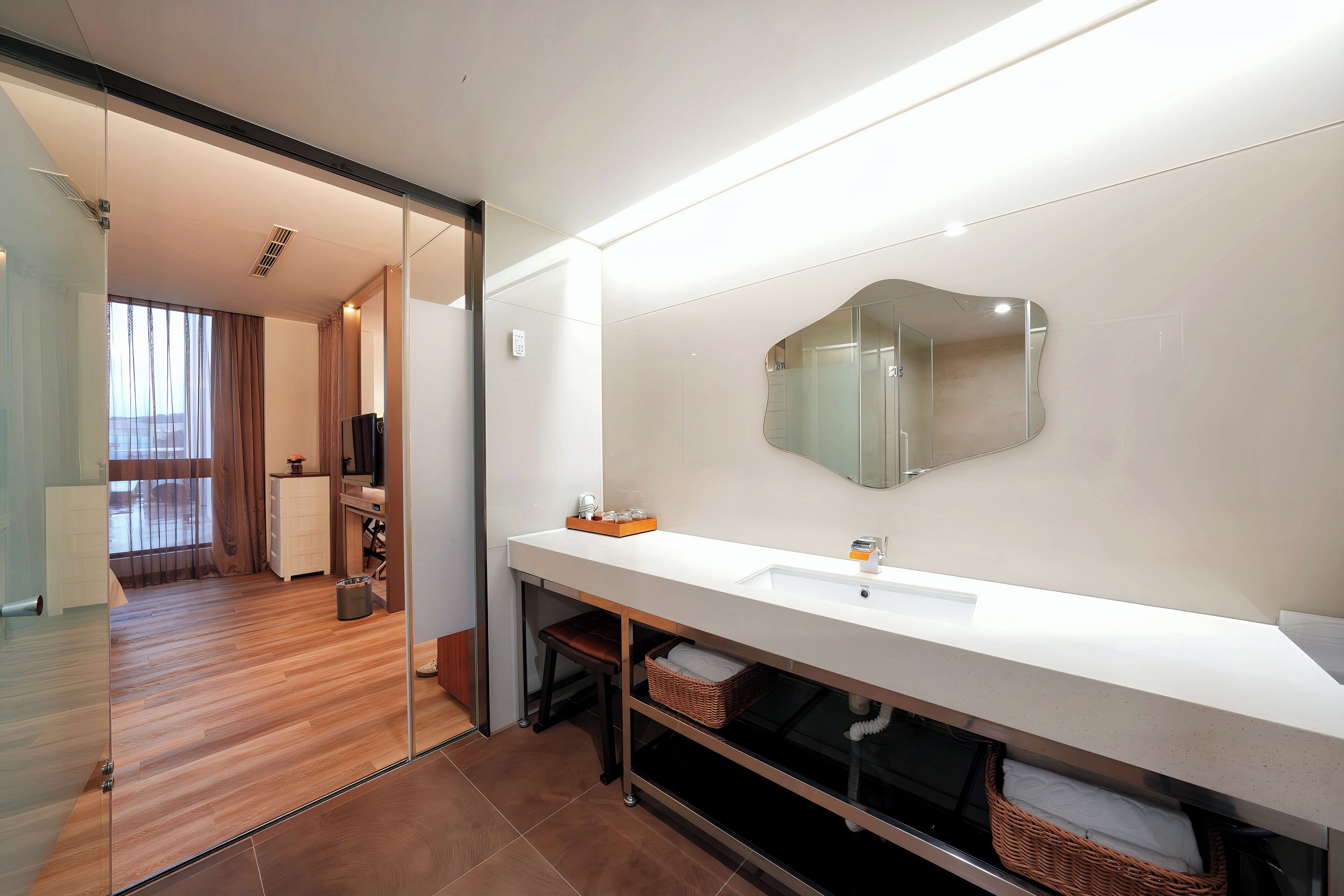 A modern bathroom with a large mirror, white countertop, and a glass partition.