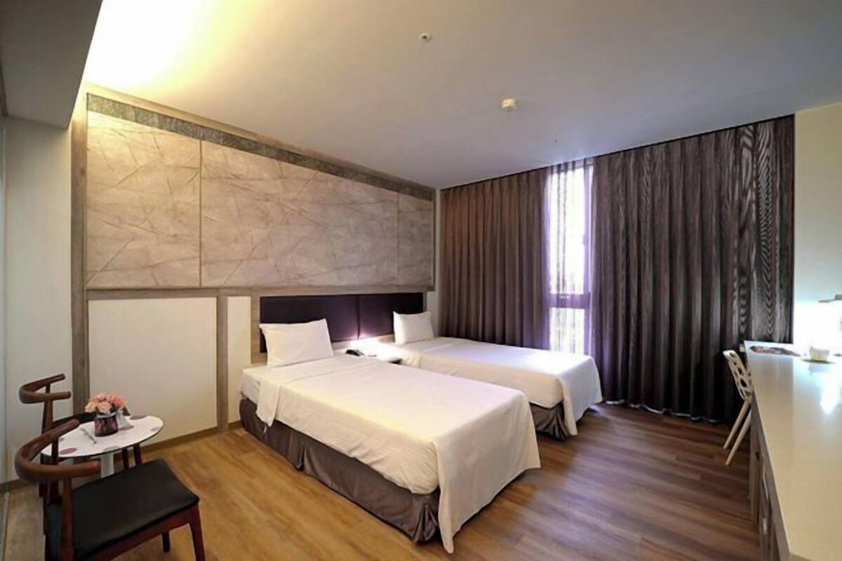 A hotel room with two beds, a desk, a chair, and a window with curtains.