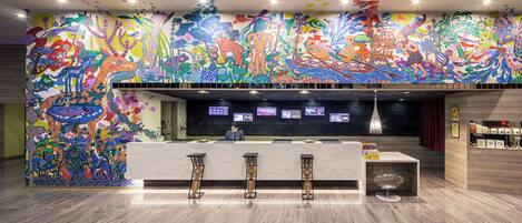 Een hotellobby met een kleurrijke muurschildering, een receptiebalie en een bar.