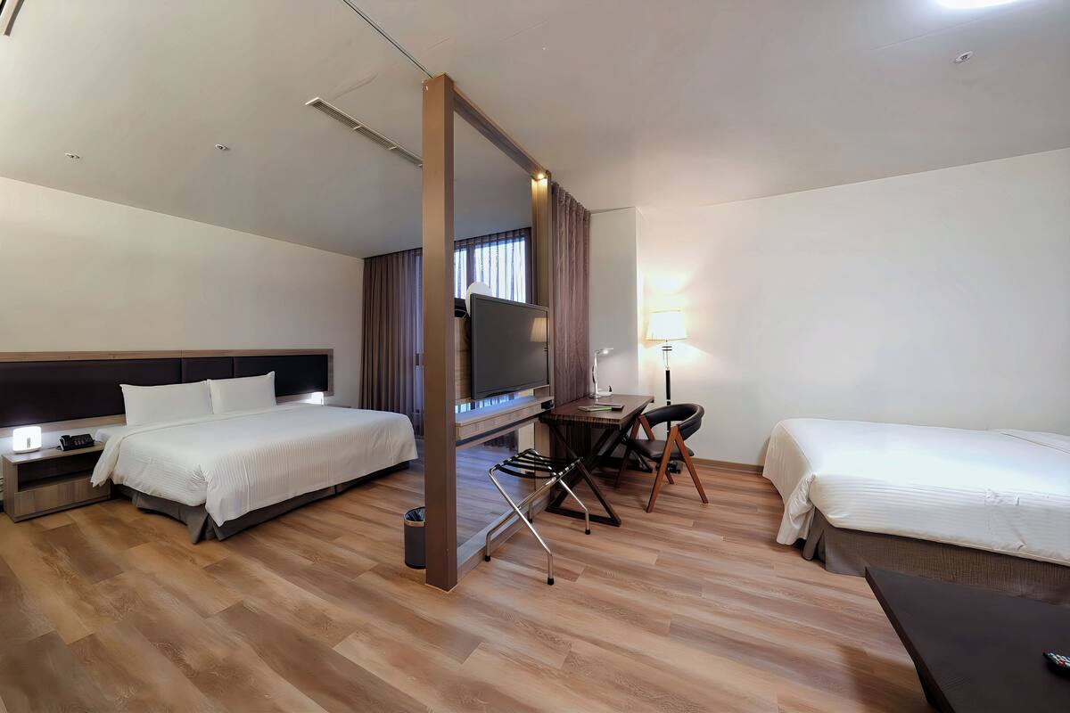 A hotel room with two beds, a desk, a chair, a TV, and a lamp.