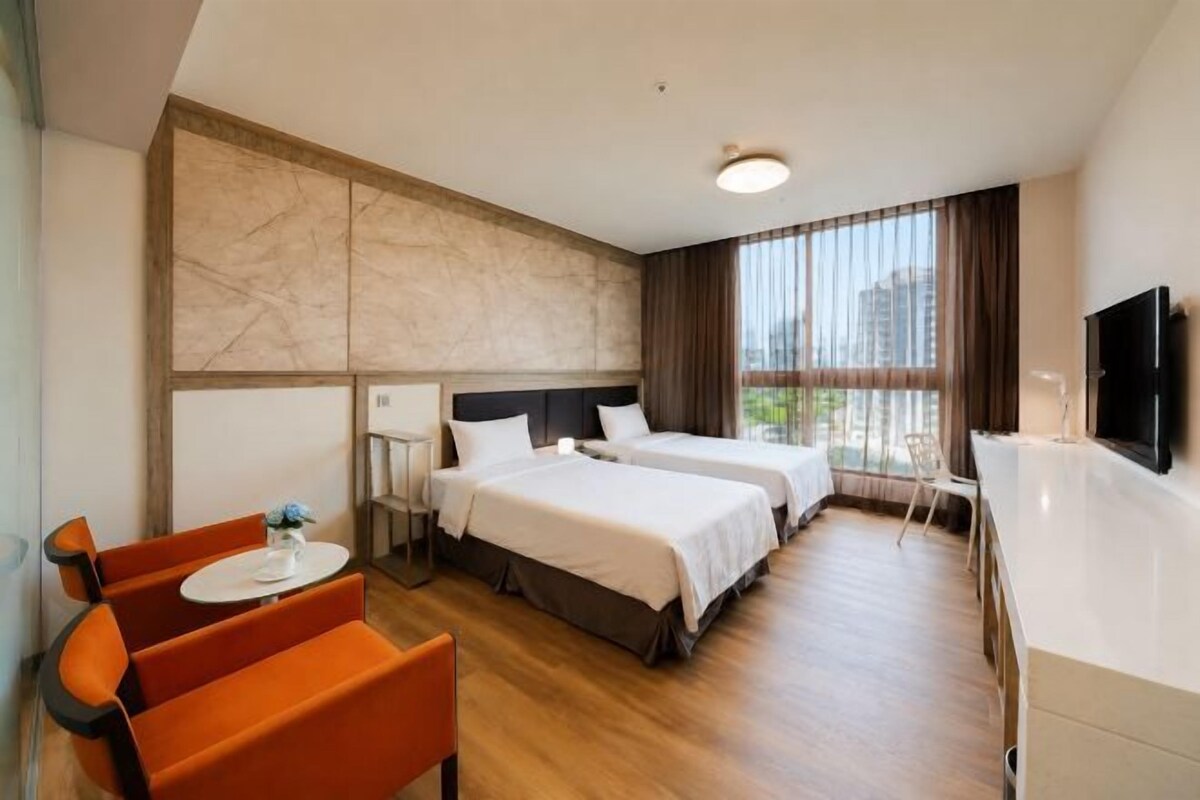 A hotel room with two beds, a desk, a chair, and a TV.