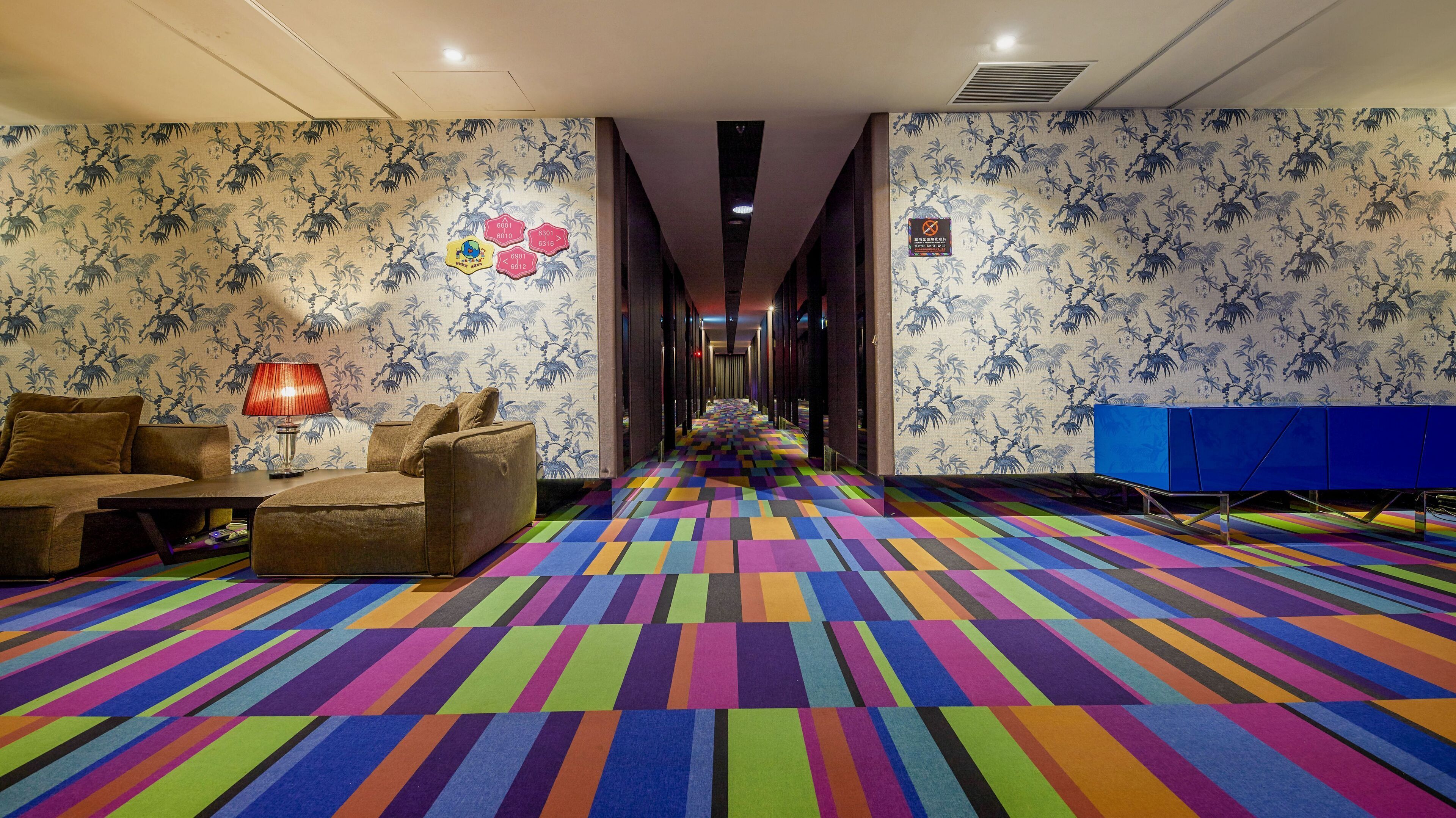 A hotel lobby with a colorful striped carpet, a sofa, a lamp, and a blue cabinet.