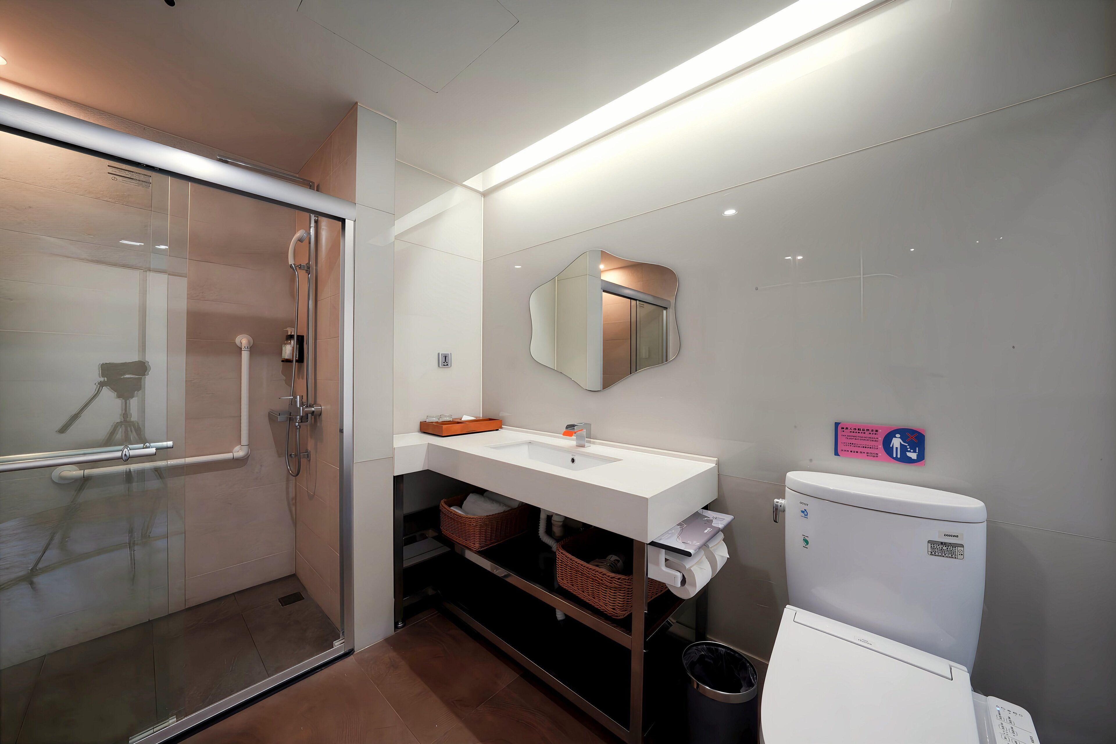 Un baño moderno con cabina de ducha de vidrio, un lavamanos blanco con espejo y un inodoro con un cubo de basura.