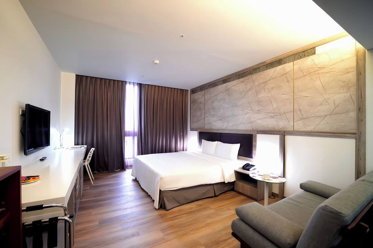 A hotel room with a bed, a desk, a chair, a sofa, and a TV.