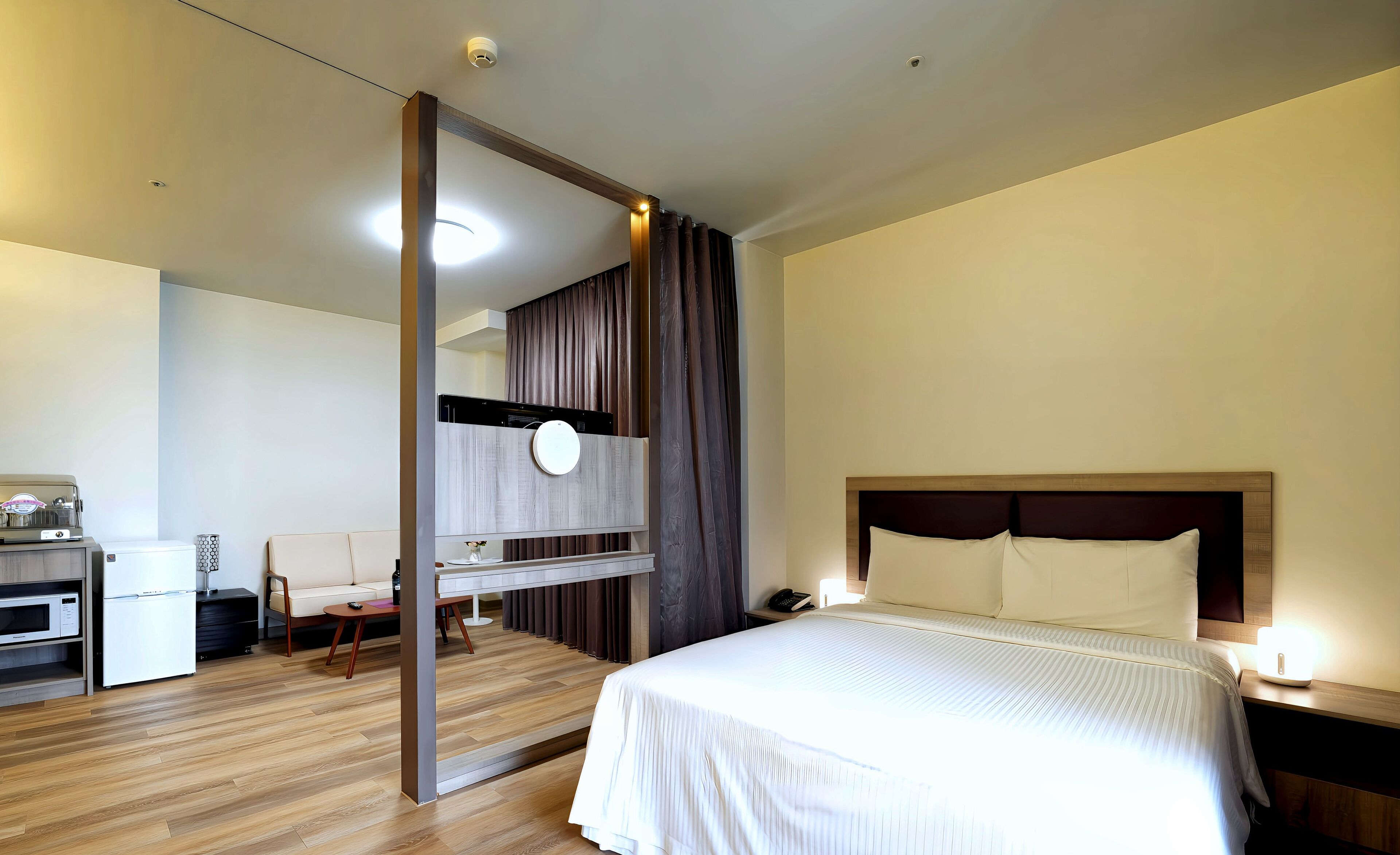Habitación de hotel moderna con una cama grande, mesita de noche y un escritorio integrado con computadora e impresora.