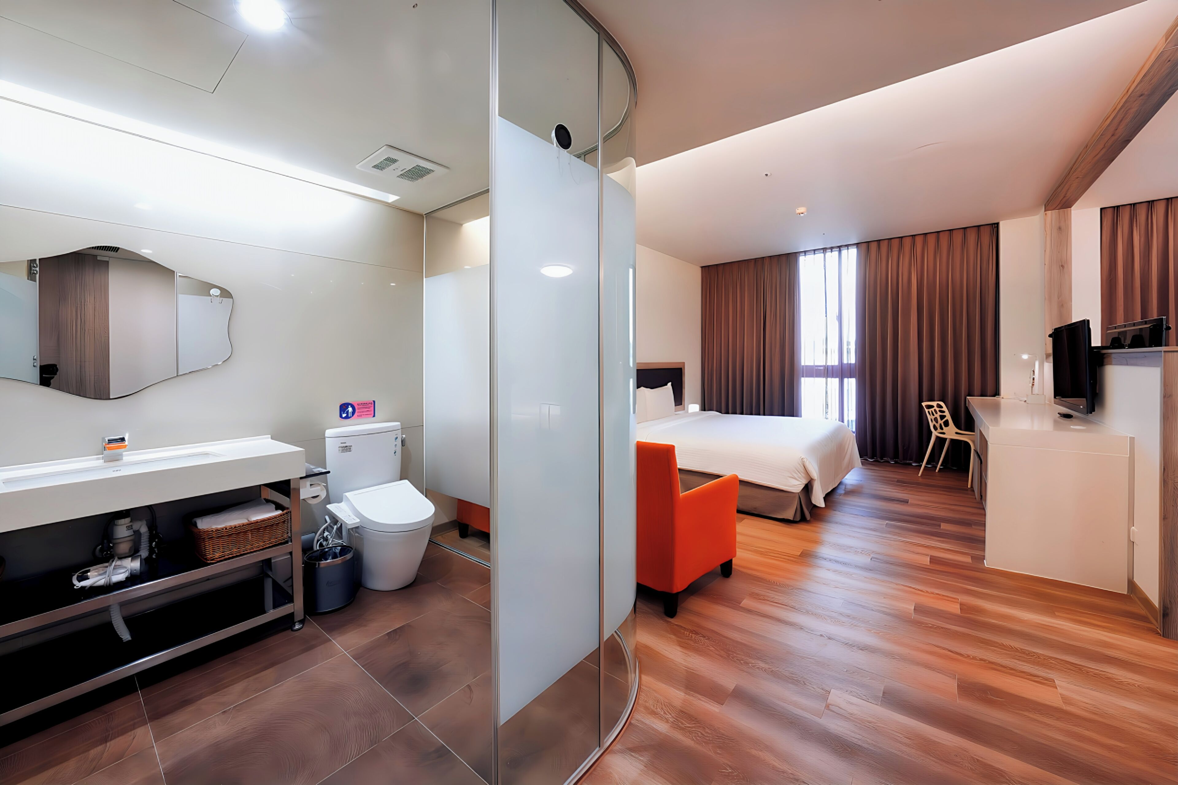 A modern hotel room with a glass partition, a bathroom with a toilet and sink, a bed with an orange chair, and a TV on a cabinet.