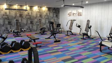 Ein Fitnessraum mit unterschiedlichen Trainingsgeräten, einem farbenfrohen Boden und einer Wand mit Bildern.