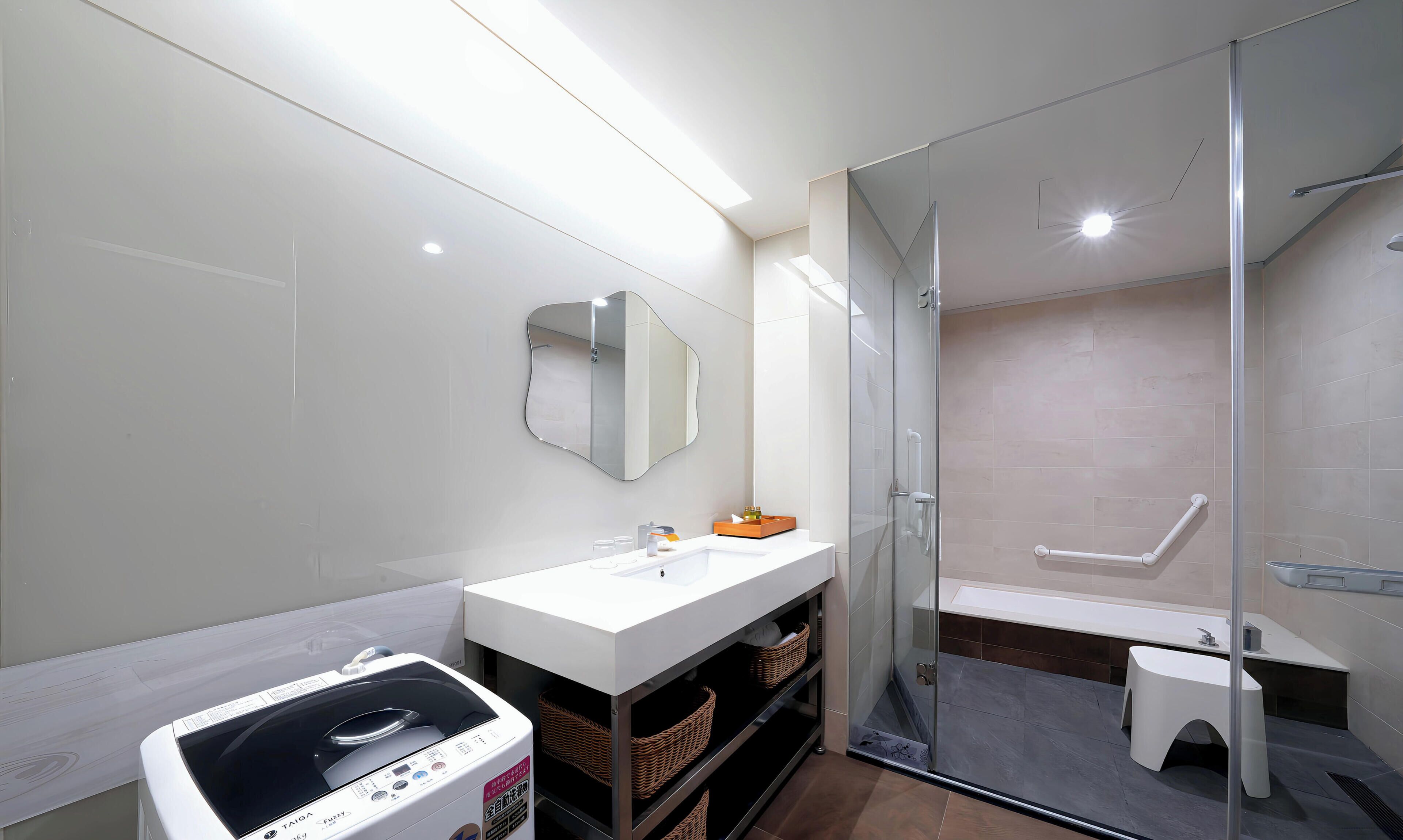 Un baño moderno con cabina de ducha de vidrio, un lavamanos blanco con espejo y una lavadora.