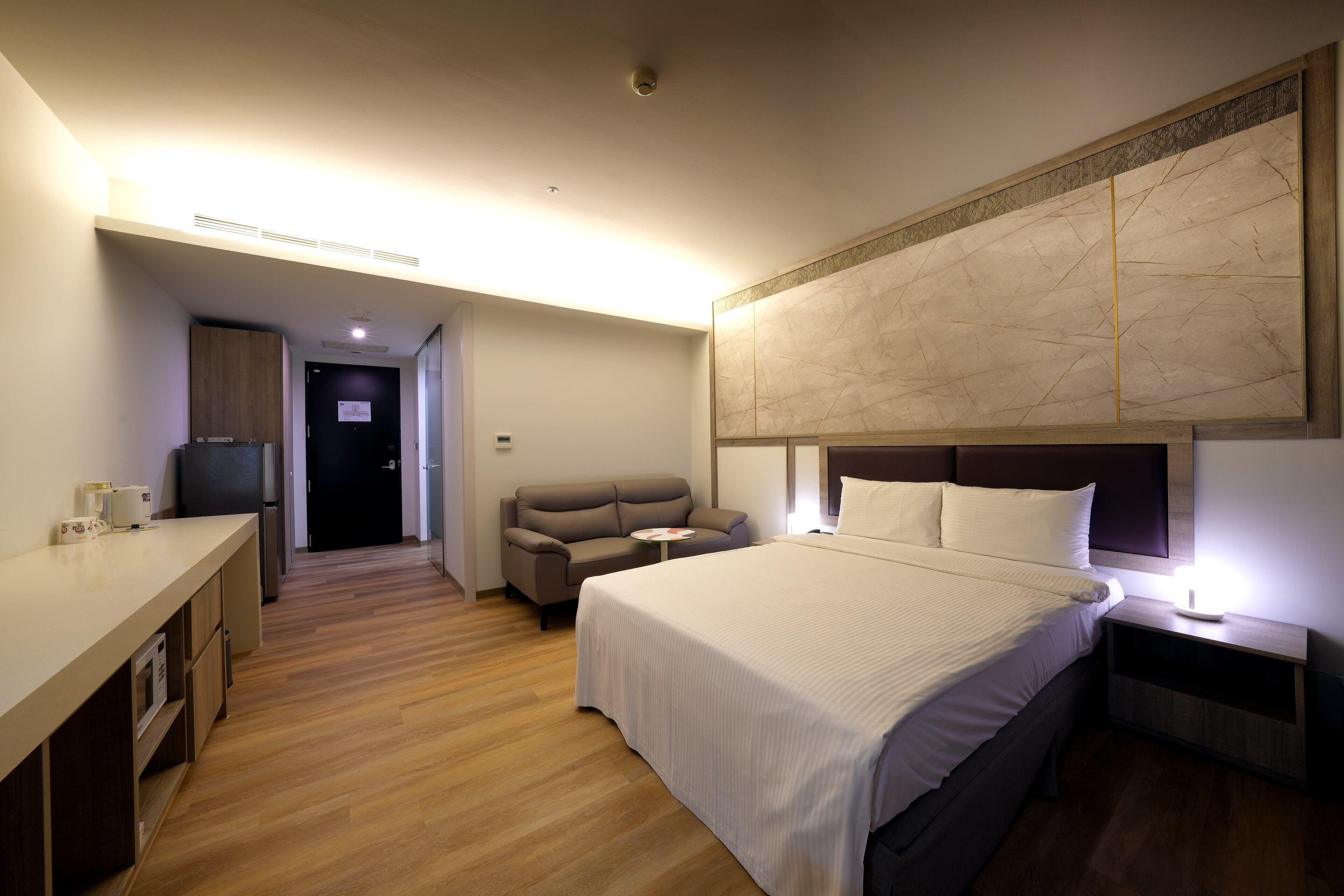 A hotel room with a bed, a sofa, a small table, and a desk with a refrigerator.
