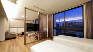 A modern hotel room with a large bed, a TV, a sofa, and a city view. - Freedom Design Hotel (Taoyuan City)