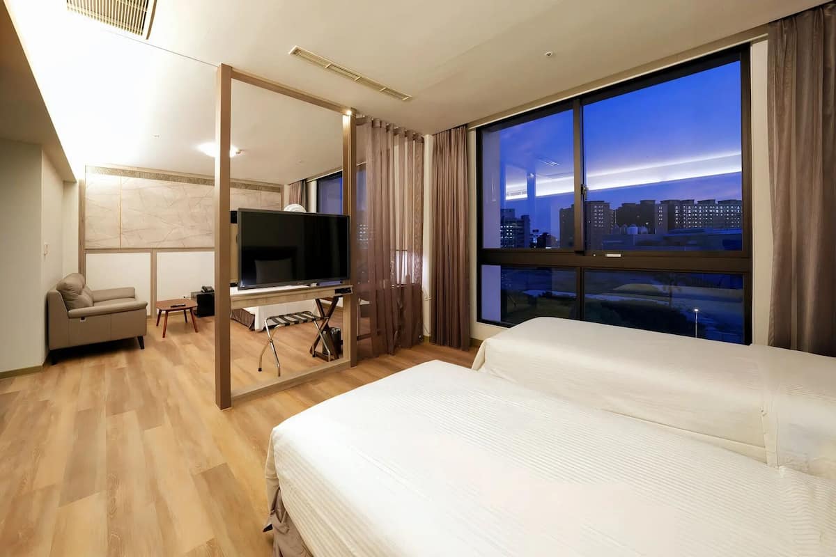 A modern hotel room with a large bed, a TV, a sofa, and a city view.
