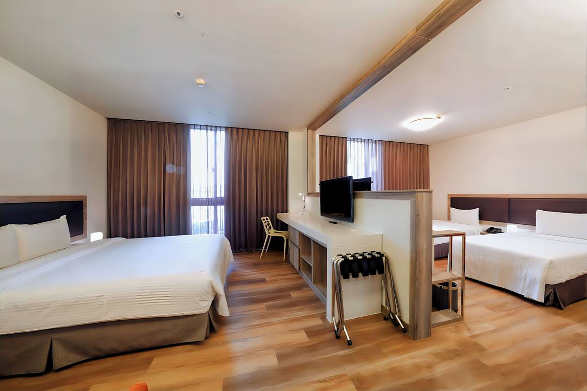 A hotel room with two beds, a desk with a TV, a chair, and a small trash bin.