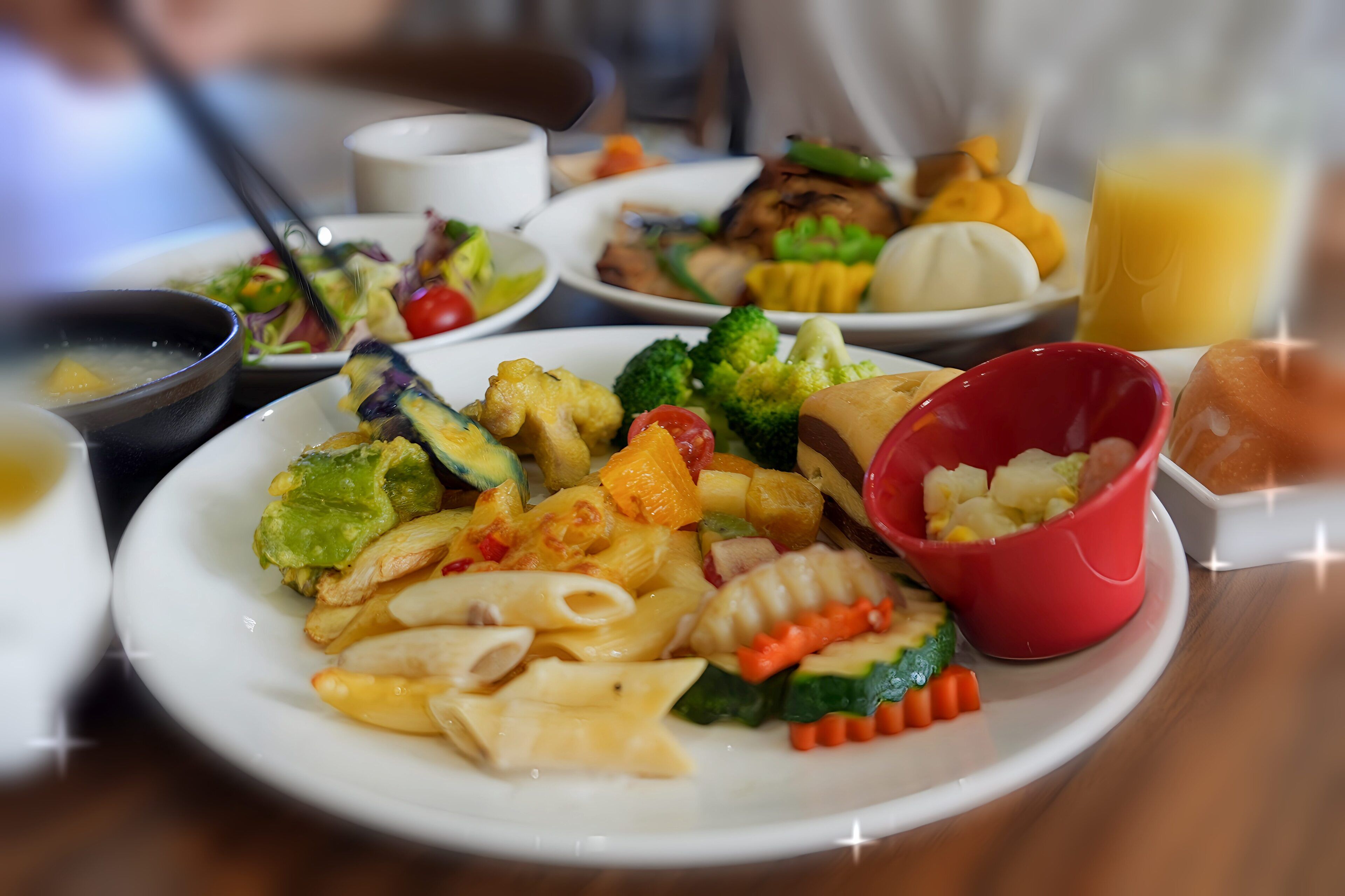 Una variedad de platos que incluyen pasta, verduras y un bol rojo de fruta sobre una mesa.
