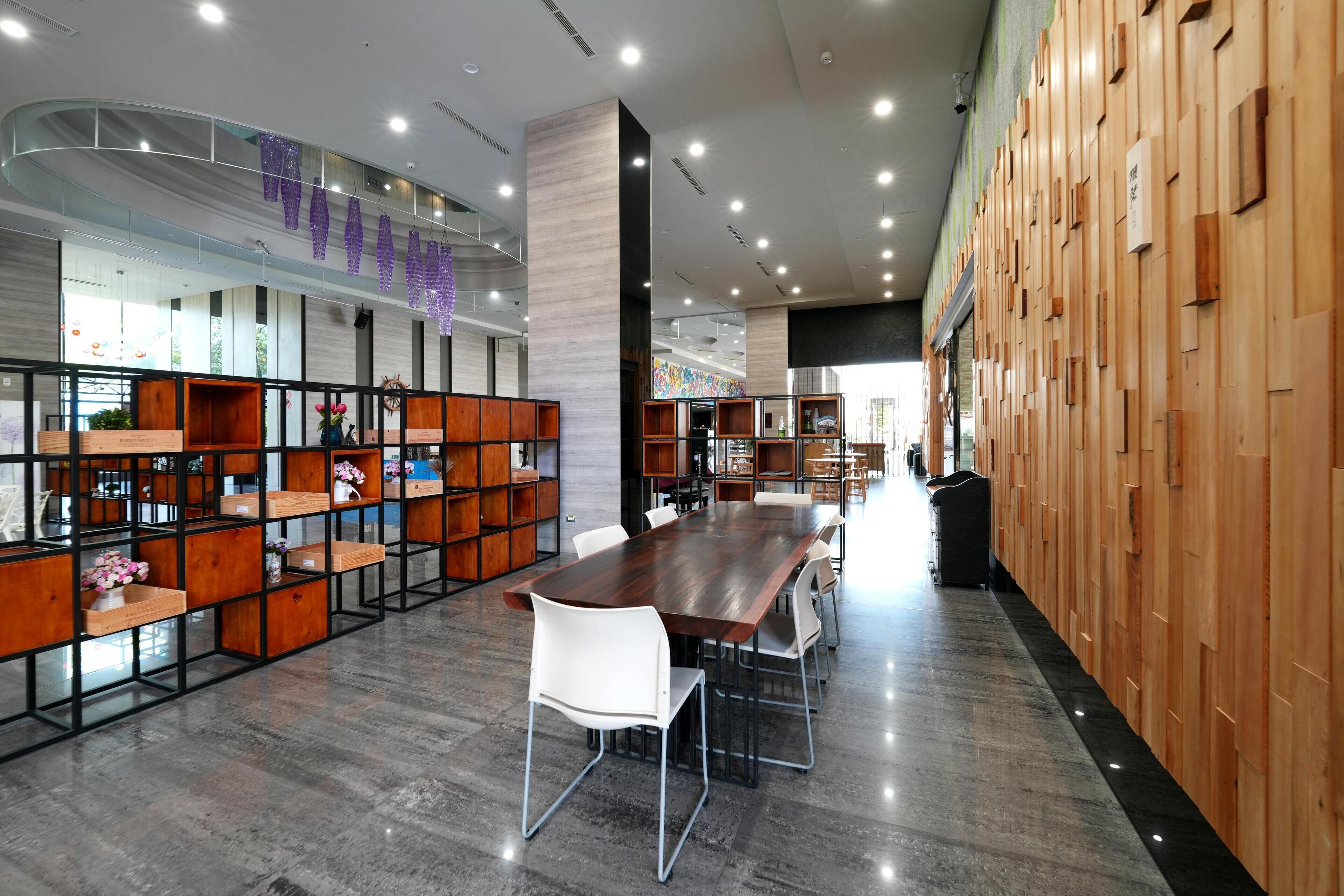 Una biblioteca moderna con una larga mesa de madera, sillas blancas y estanterías llenas de libros y objetos decorativos.