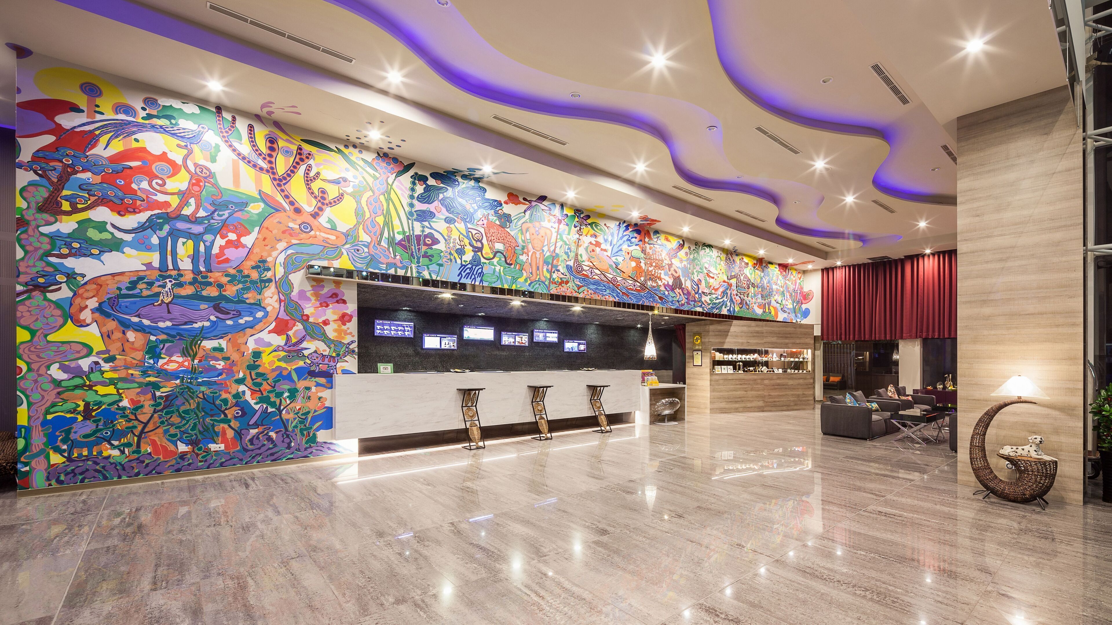 A modern lobby with a colorful mural, a reception desk, and a seating area with a red curtain backdrop.
