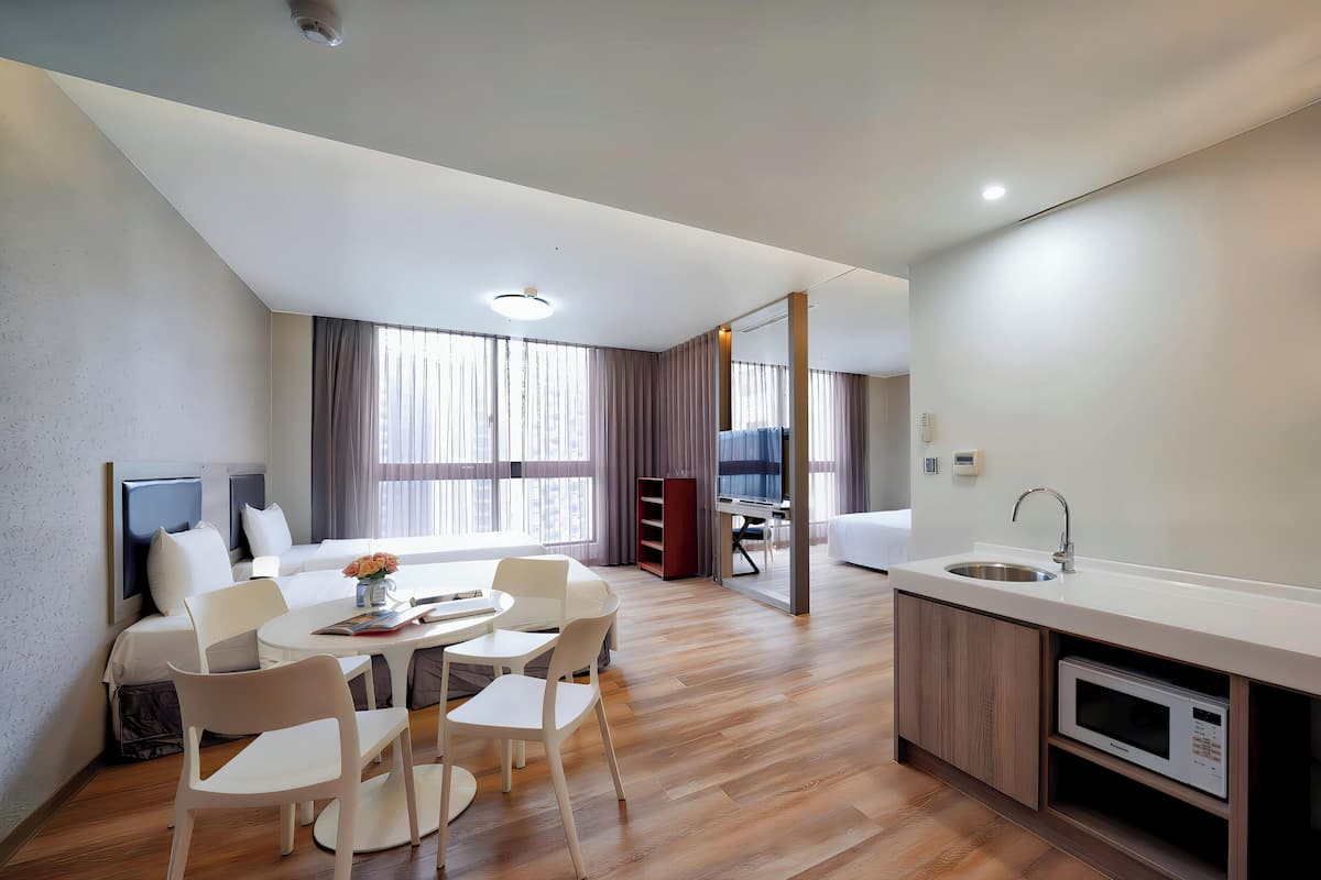 A modern hotel room with a dining area, a kitchenette, and a large window with curtains.