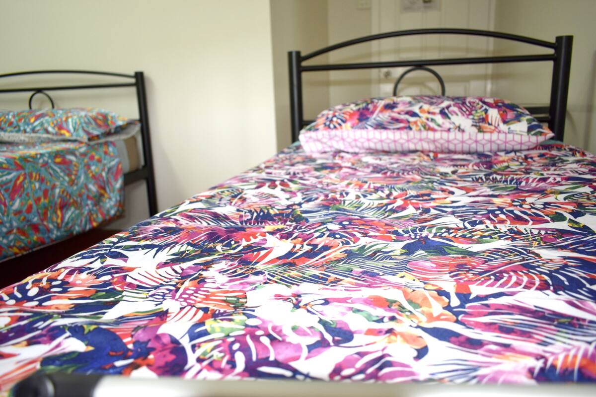 Ein Bett mit farbenfroher Blumenbettdecke, einem schwarzen Metall-Kopfende und passendem Kopfkissen.