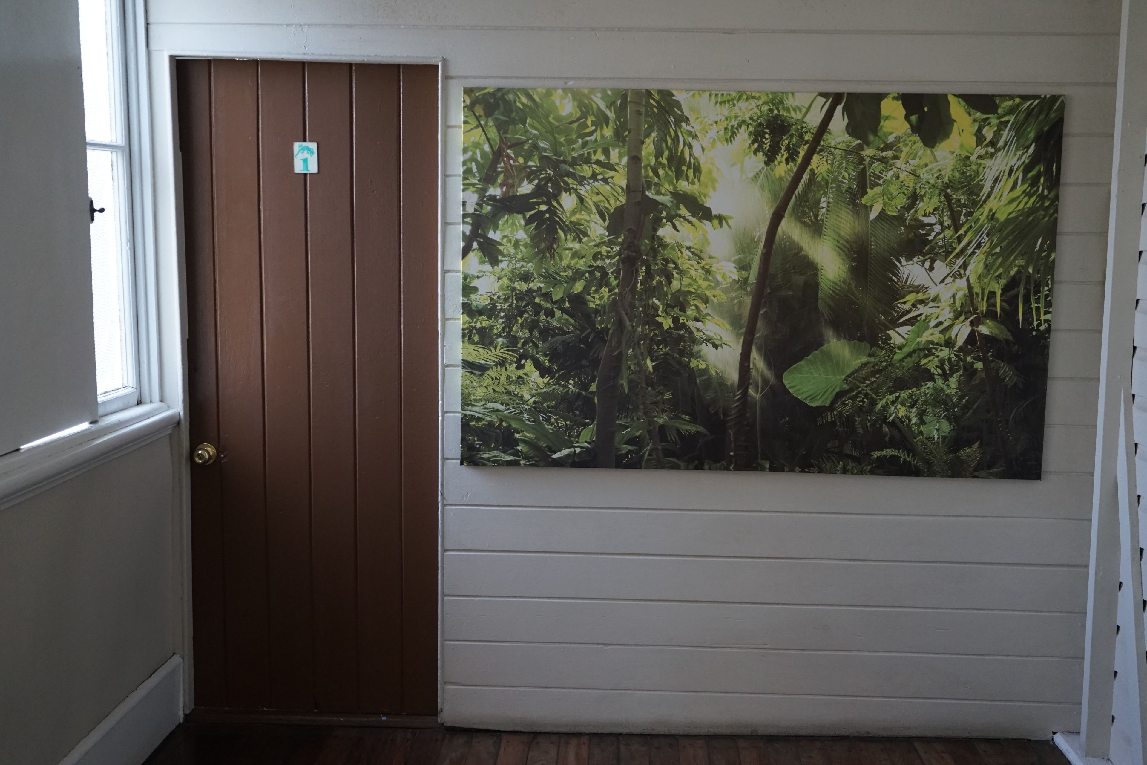 A room with a brown door and a large forest-themed painting on the wall.
