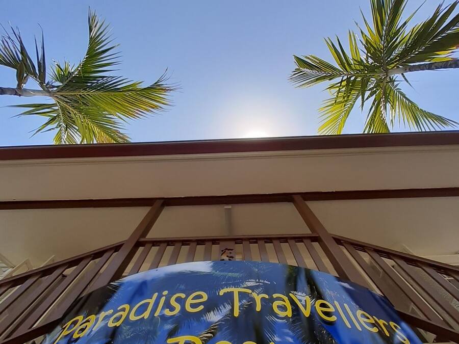 A sign for Paradise Travellers Rest with palm trees and a clear sky in the background.