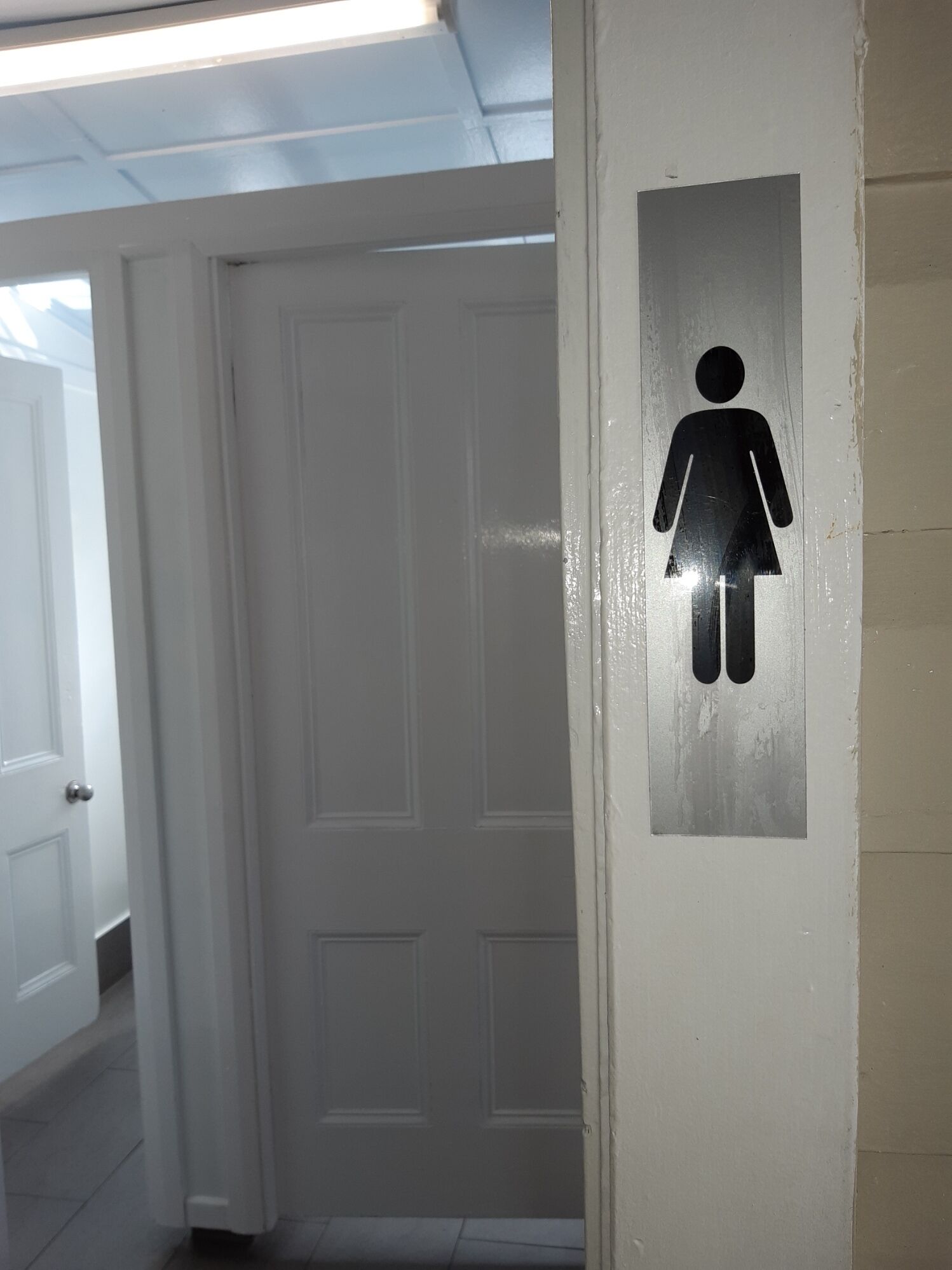 Un panneau indiquant les toilettes, avec un symbole féminin, sur un mur blanc.