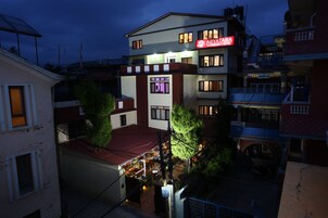 Un hotel de varios pisos con fachada roja y blanca, múltiples balcones y un área de restaurante visible.