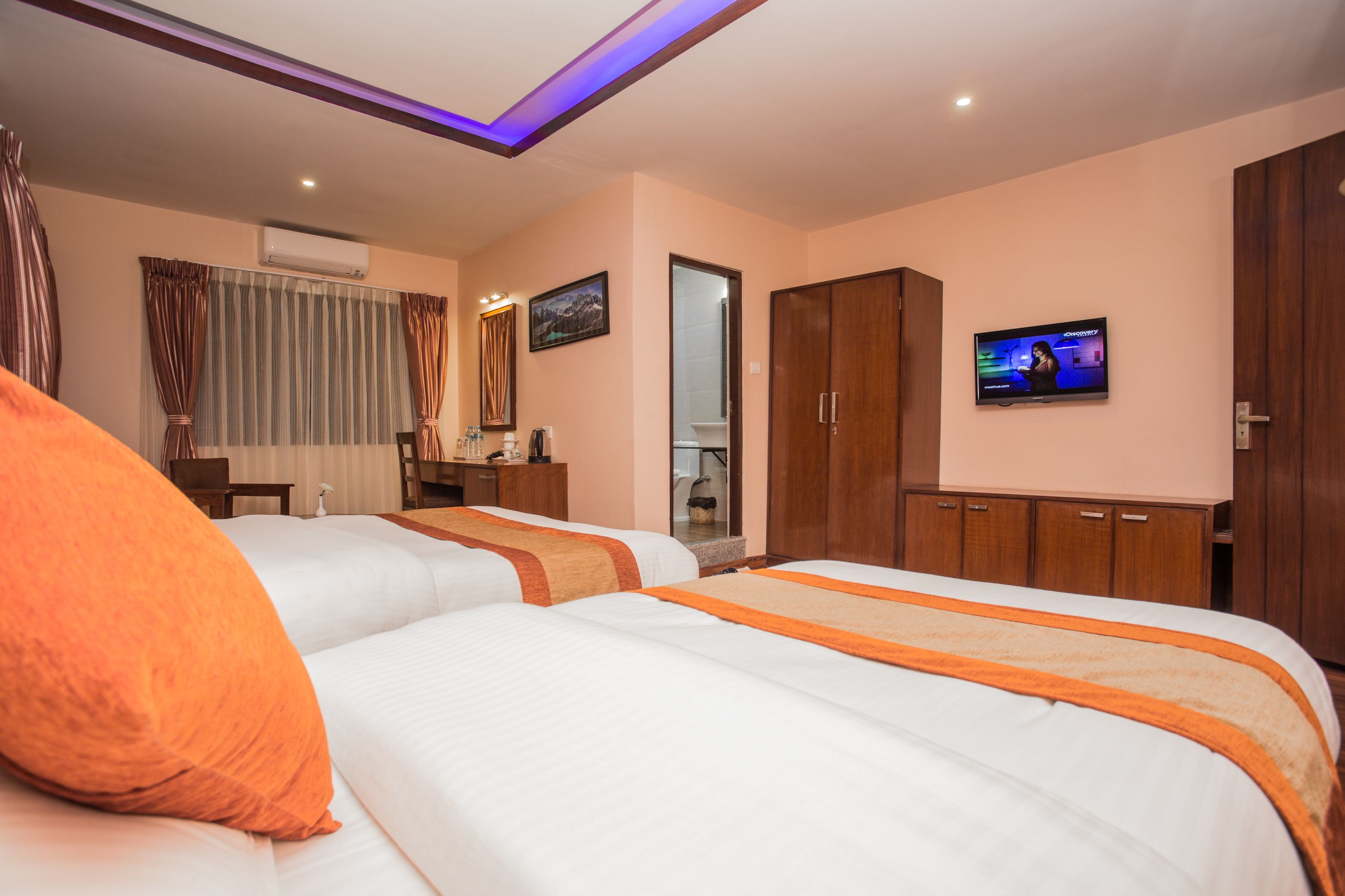 A hotel room with two beds, a TV, a wardrobe, and a desk with a chair.