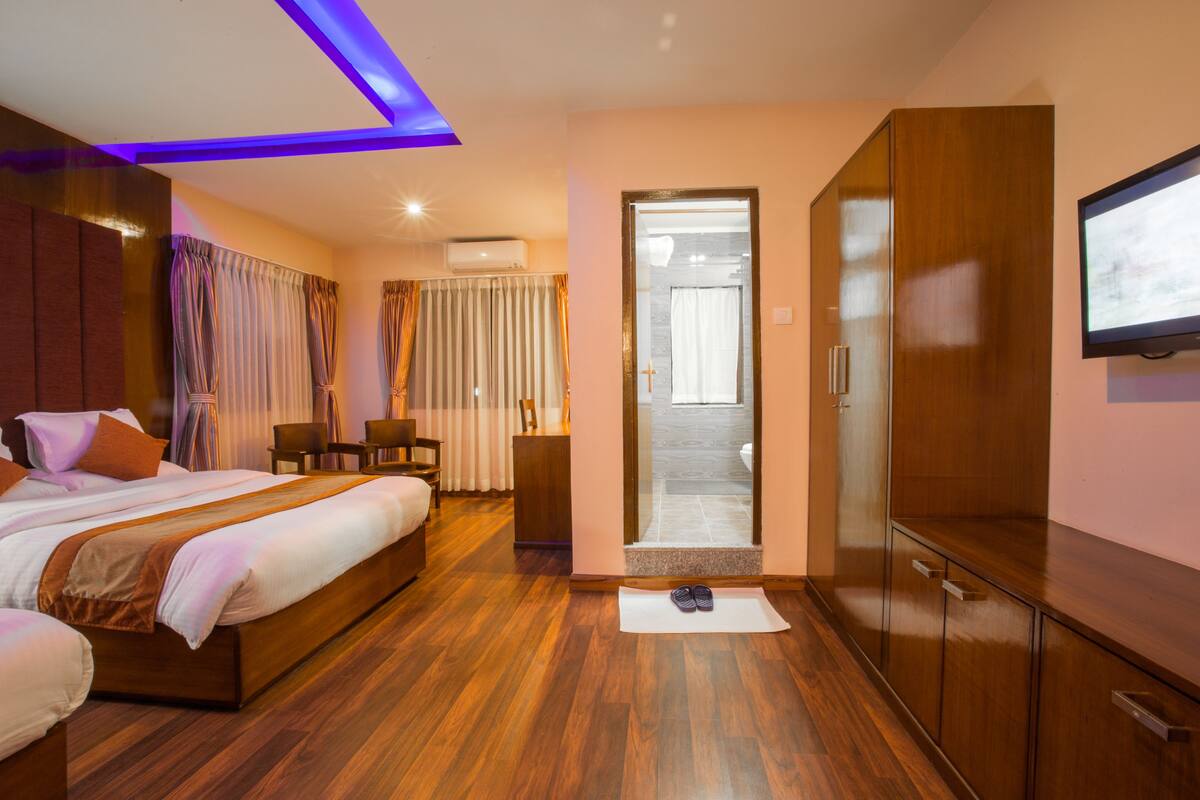 A hotel room with a wooden bed, a TV, a wardrobe, and a bathroom visible through an open door.