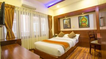 Habitación de hotel con una cama de madera, un escritorio, una silla, un aire acondicionado y dos cuadros en la pared.