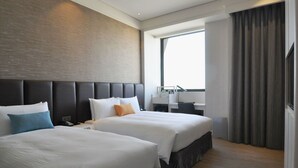 Hotellihuone, jossa on kaksi sänkyä, työpöytä ja suuri ikkuna.
