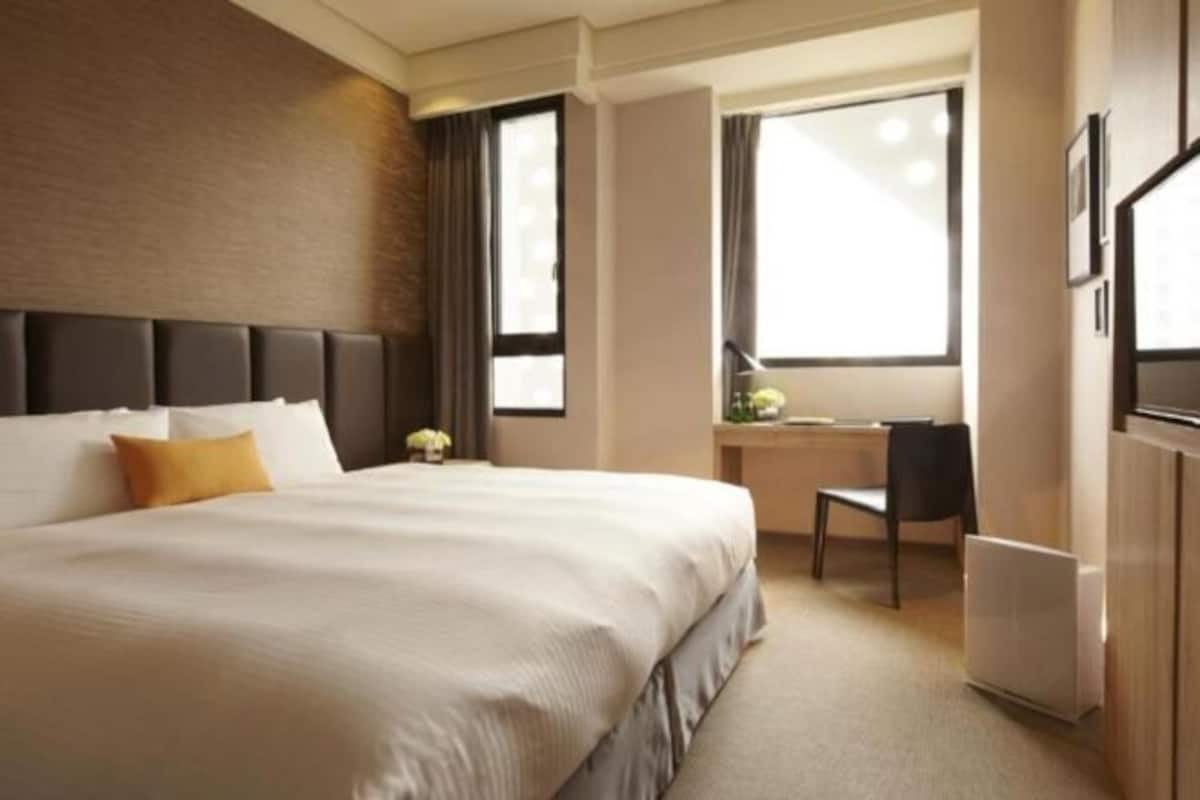 A hotel room with a large bed, a desk, and a chair.