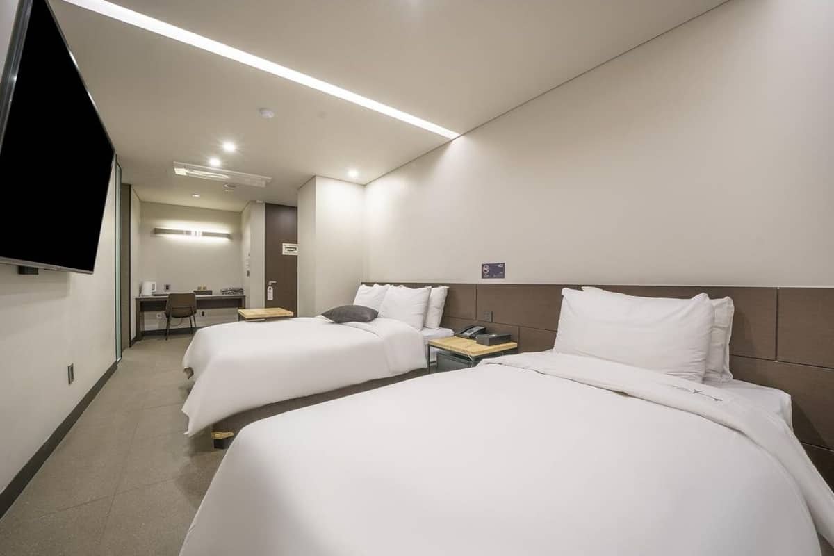 A hotel room with two beds, a desk, a chair, and a TV.