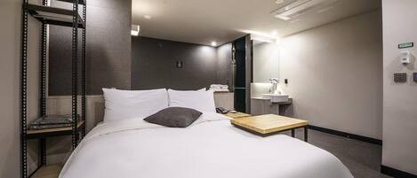 Hotellihuone, jossa on sänky, yöpöytä, peili, hylly ja seinälle asennettu ilmastointilaite.