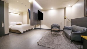 Ein modernes Hotelzimmer mit Bett, einer Couch, einem an der Wand befestigten Fernseher und einem kleinen Tisch.