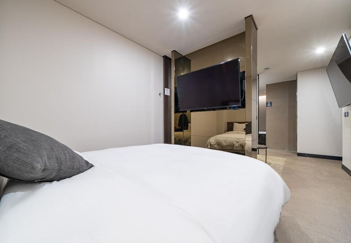 Une chambre d’hôtel moderne avec un grand lit, un téléviseur à écran plat fixé au mur et une petite table.