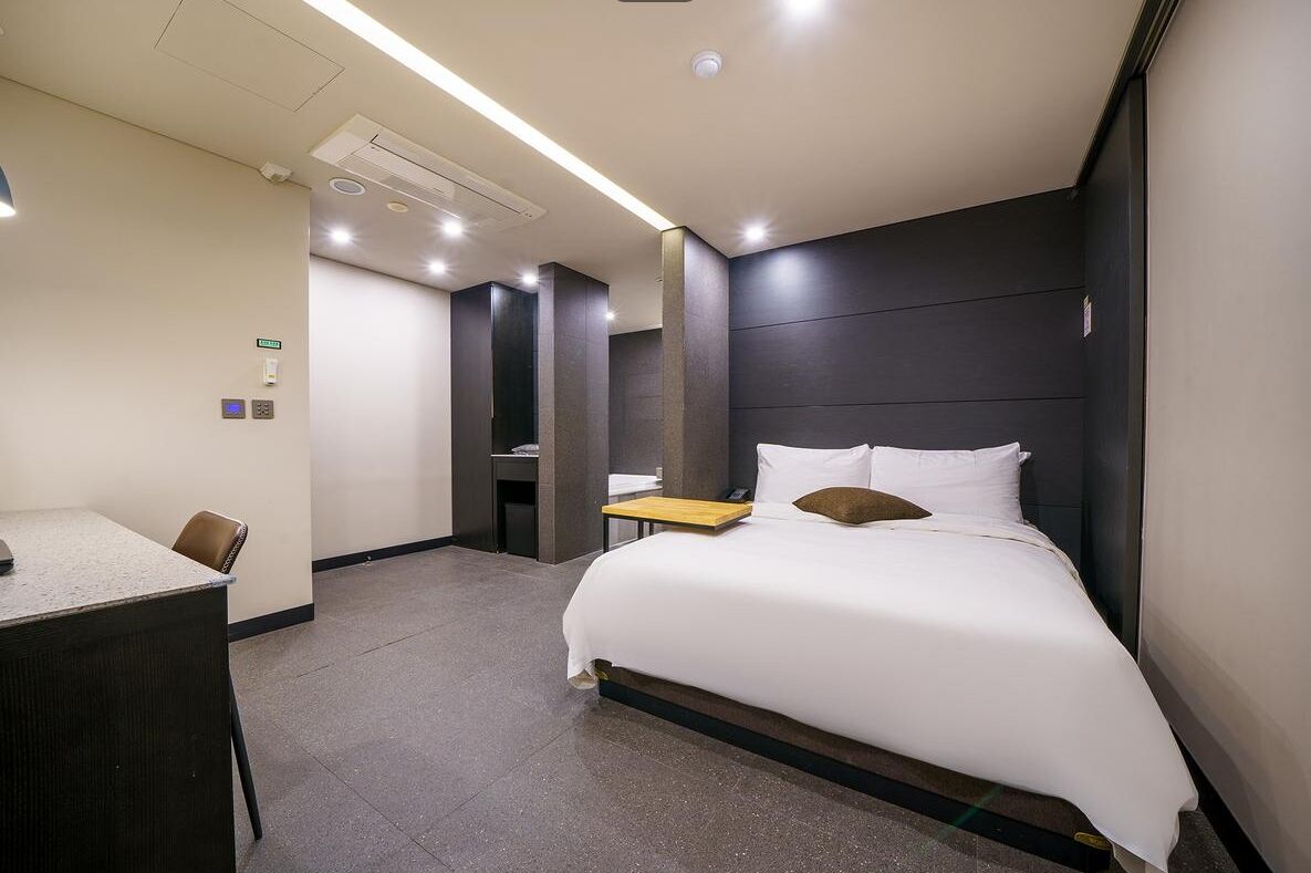 Una habitación de hotel moderna con una cama grande, un escritorio y una silla. Hay una pequeña mesa y un espejo en la pared.