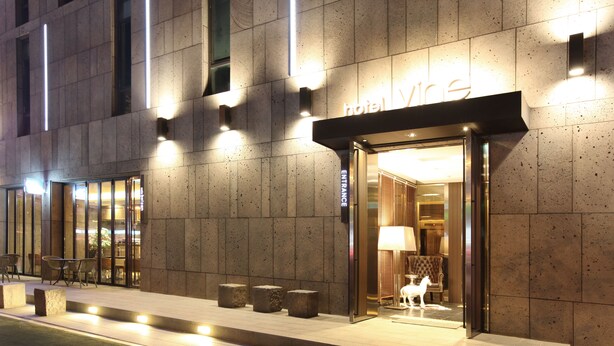 Ein Hotel mit moderner Fassade, beleuchteter Beschilderung und Außenbestuhlung.