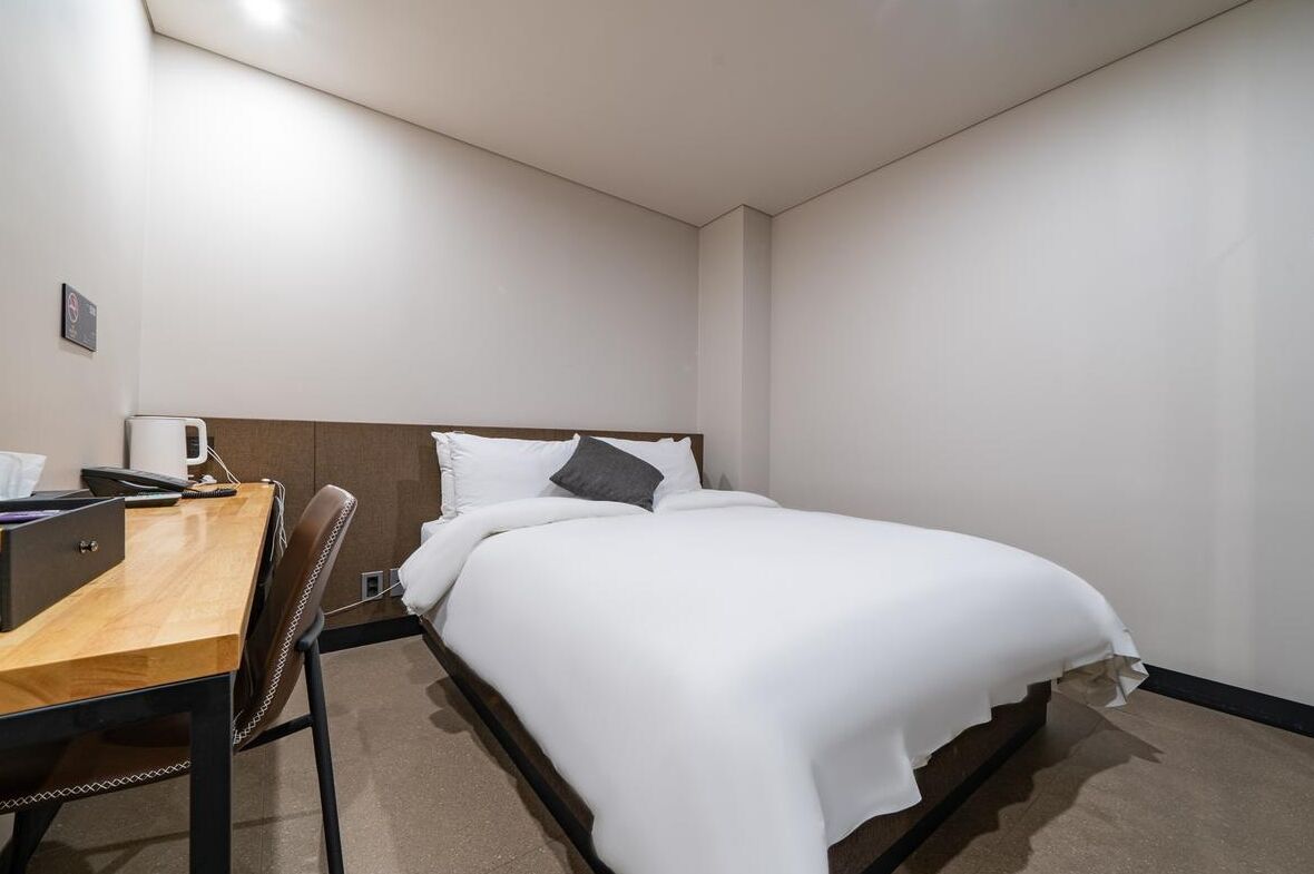 A hotel room with a single bed, a wooden desk, and a chair.