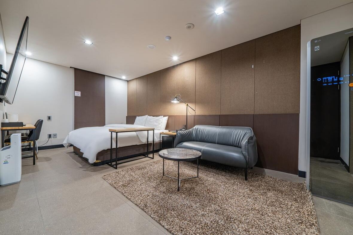Une chambre d’hôtel moderne comprenant un lit, un canapé en cuir, une petite table ronde et un bureau avec une chaise.