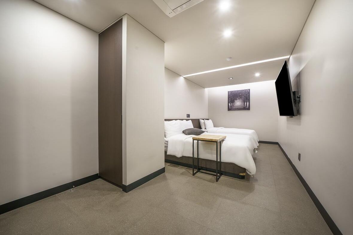 A hotel room with a bed, a small table, a wall-mounted TV, and a painting on the wall.