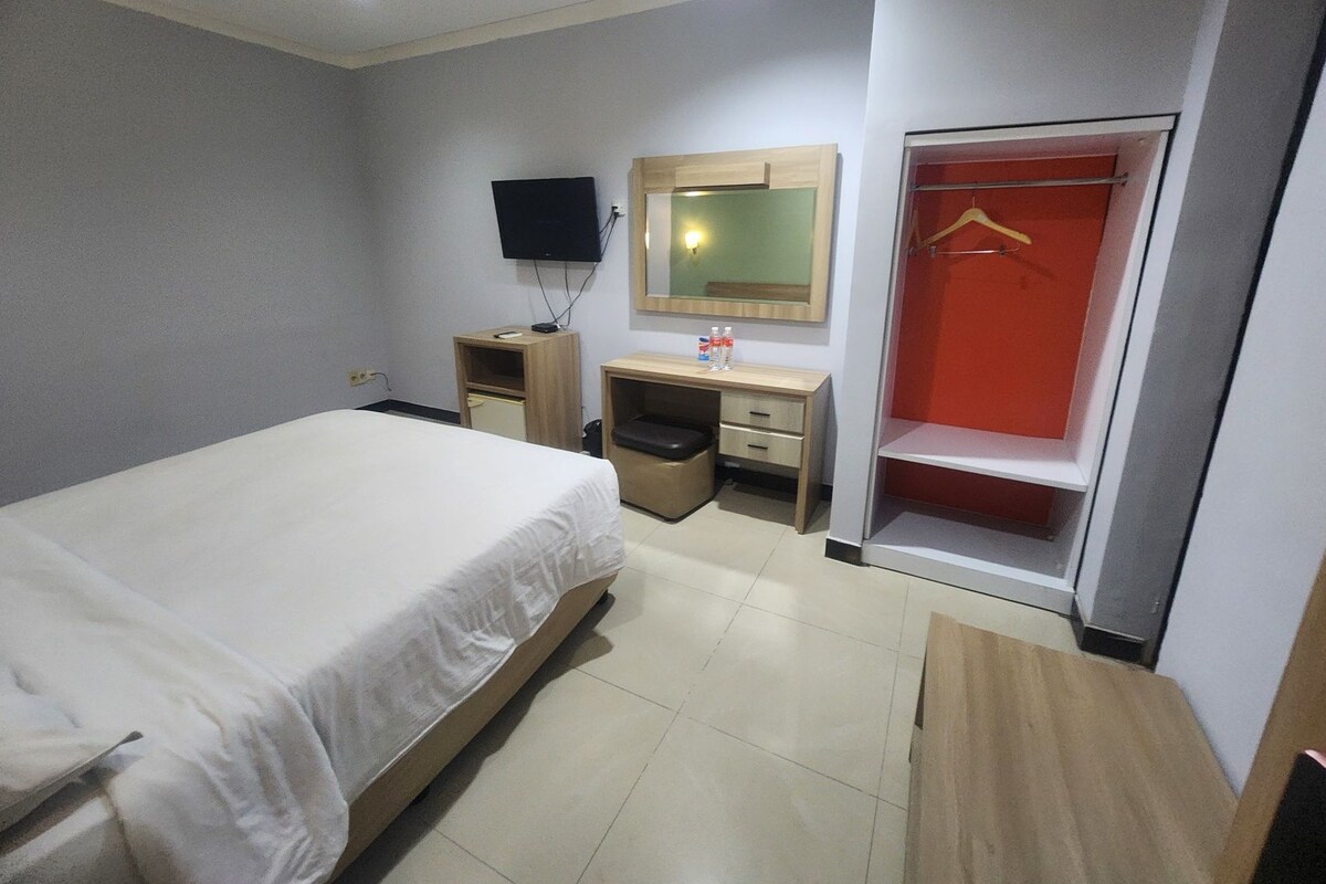 Ein Hotelzimmer mit einem Bett, einem Schreibtisch, einem Spiegel, einem Fernseher und einem Kleiderschrank.