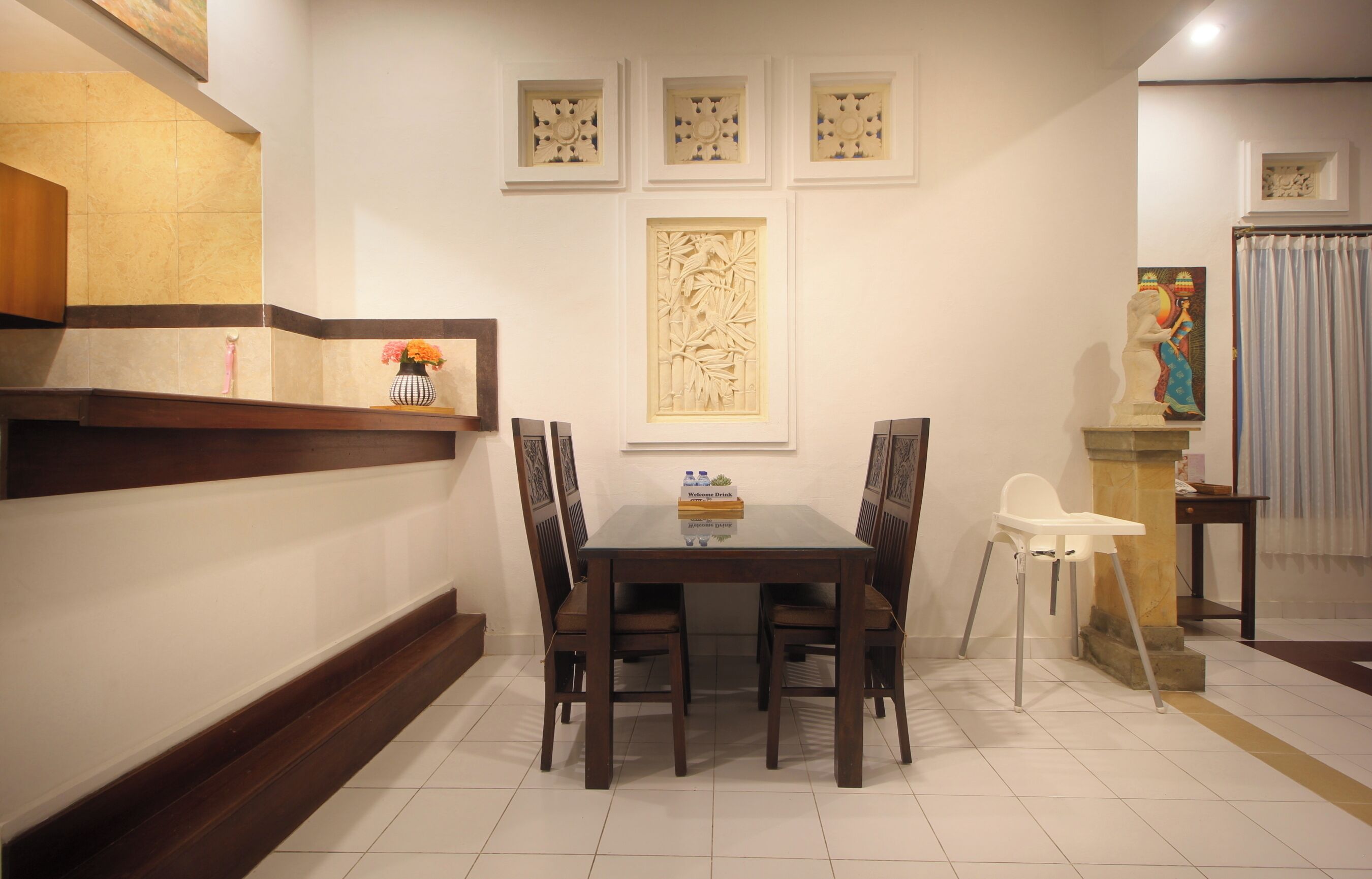 A dining area with a wooden table, four chairs, a decorative wall panel, and a statue.