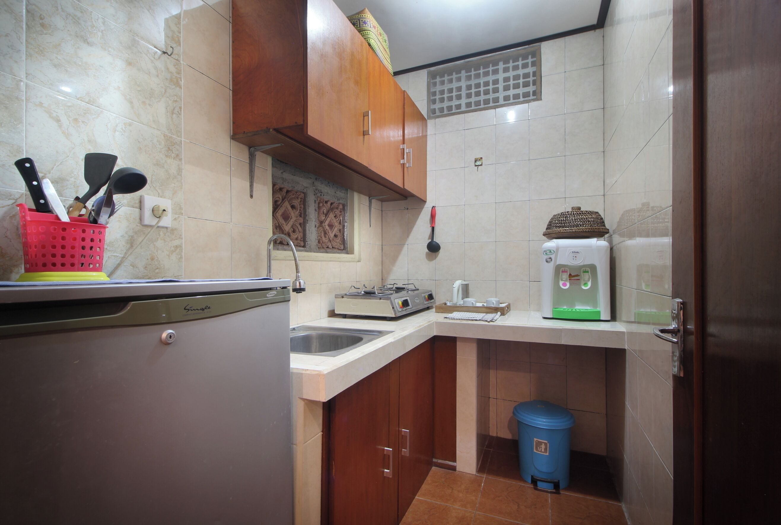 Una cocina compacta con refrigerador, estufa, lavaplatos y un cubo de basura azul.